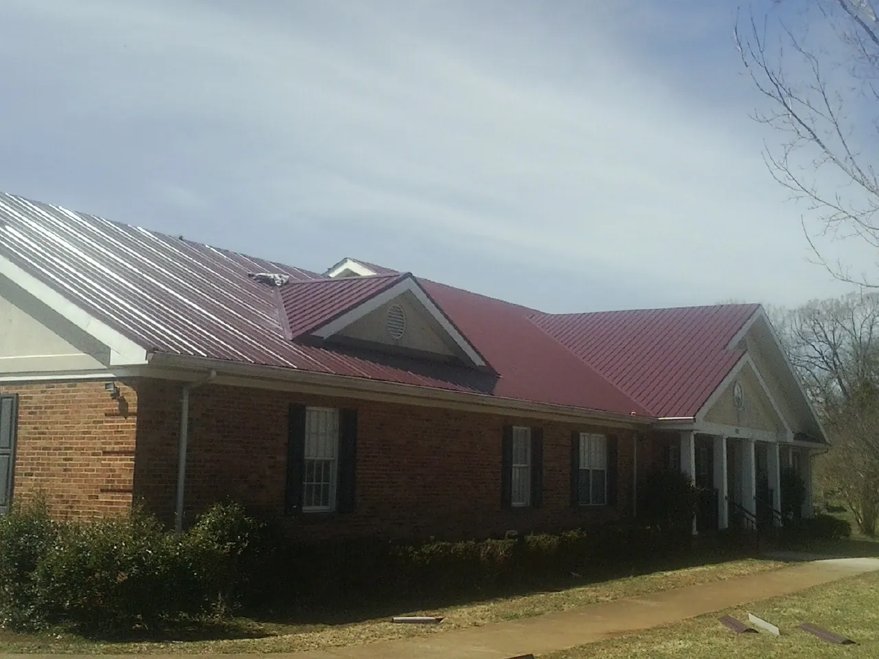 Red metal roof with gabled entries on a long brick building, from a Hail Damage Roof Repair job in Dover AFB