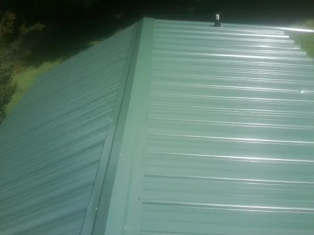 New green metal panels meeting at the ridge of a roof — Flat Roof Repair work by our crew in Dover AFB