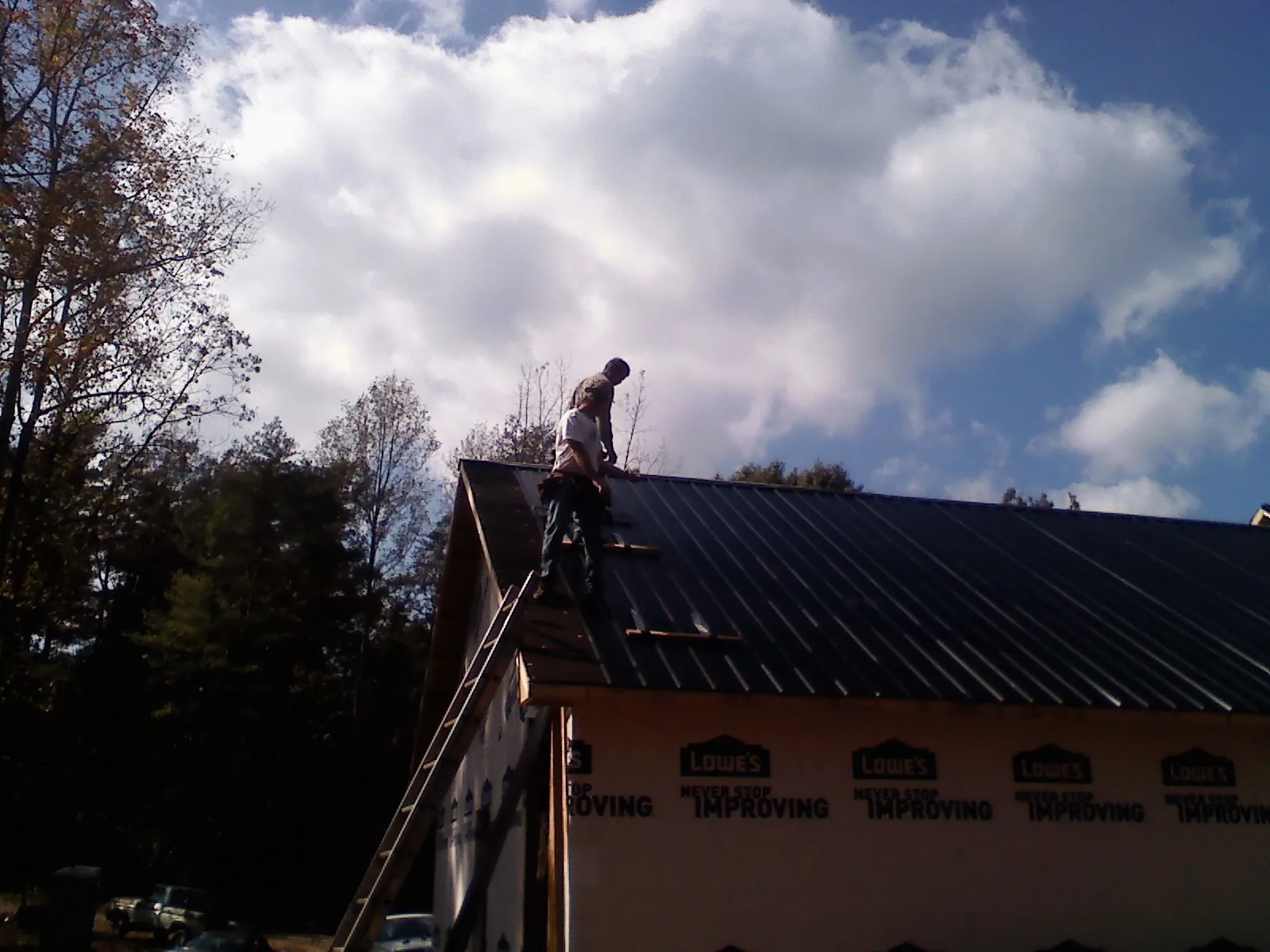 Roofer fastening dark metal panels high against a cloudy sky, from a Roof Inspection job in Dover AFB